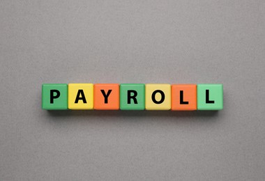 Word Payroll made of colorful wooden cubes with letters on grey background, top view