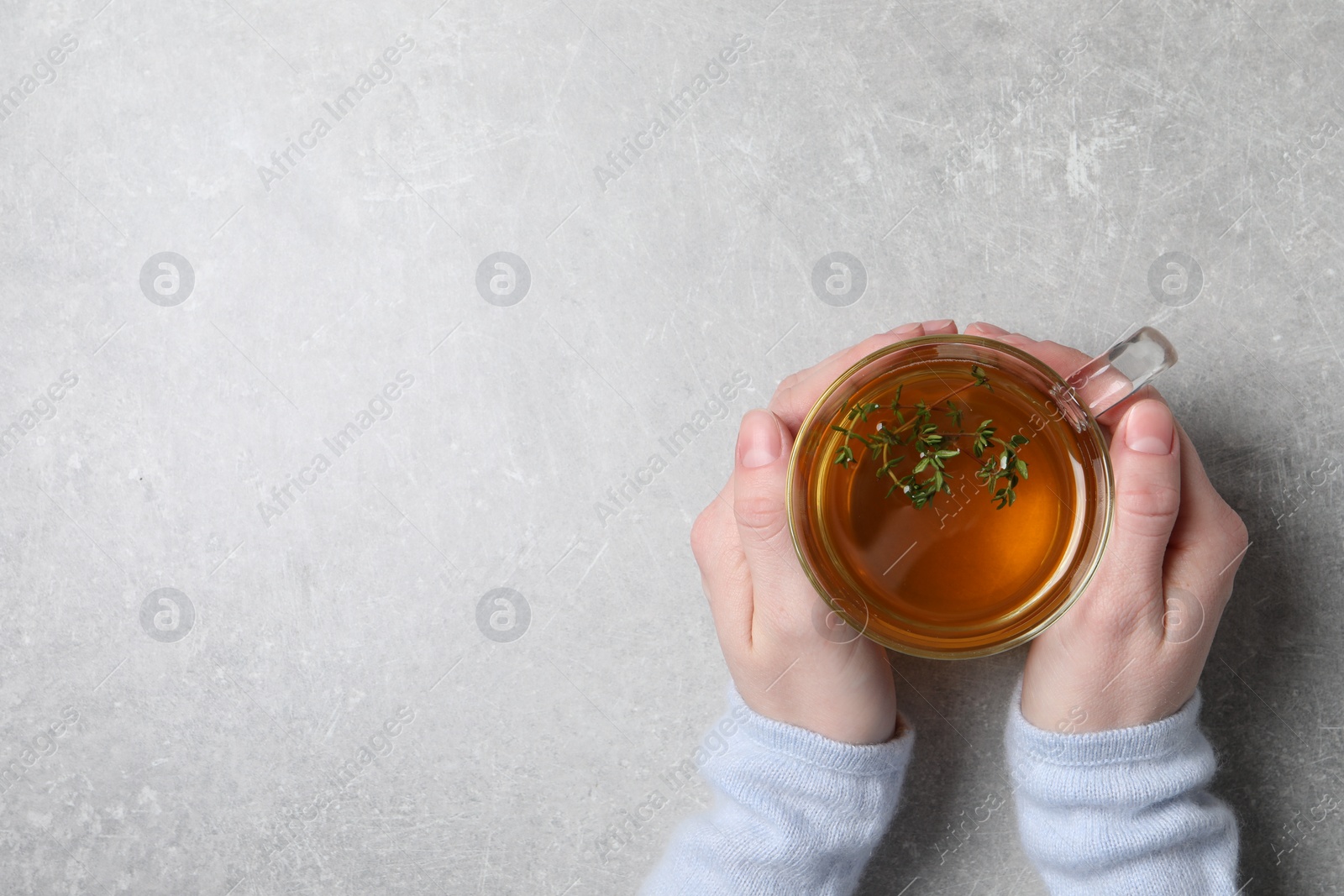 Photo of Woman holding cup of tasty herbal tea with thyme at light grey table, top view. Space for text