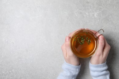 Photo of Woman holding cup of tasty herbal tea with thyme at light grey table, top view. Space for text