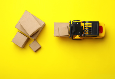 Photo of Top view of toy forklift with boxes on yellow background. Logistics and wholesale concept