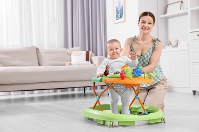 Photo of Cute boy making first steps with baby walker. Happy mother and her little son spending time together at home, space for text