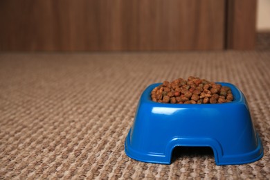 Photo of Dry pet food in feeding bowl on soft carpet indoors. Space for text