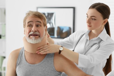 Orthopedist applying cervical collar onto patient's neck in clinic