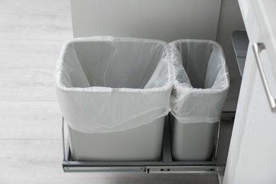 Photo of Open cabinet with empty trash bins for separate waste collection in kitchen