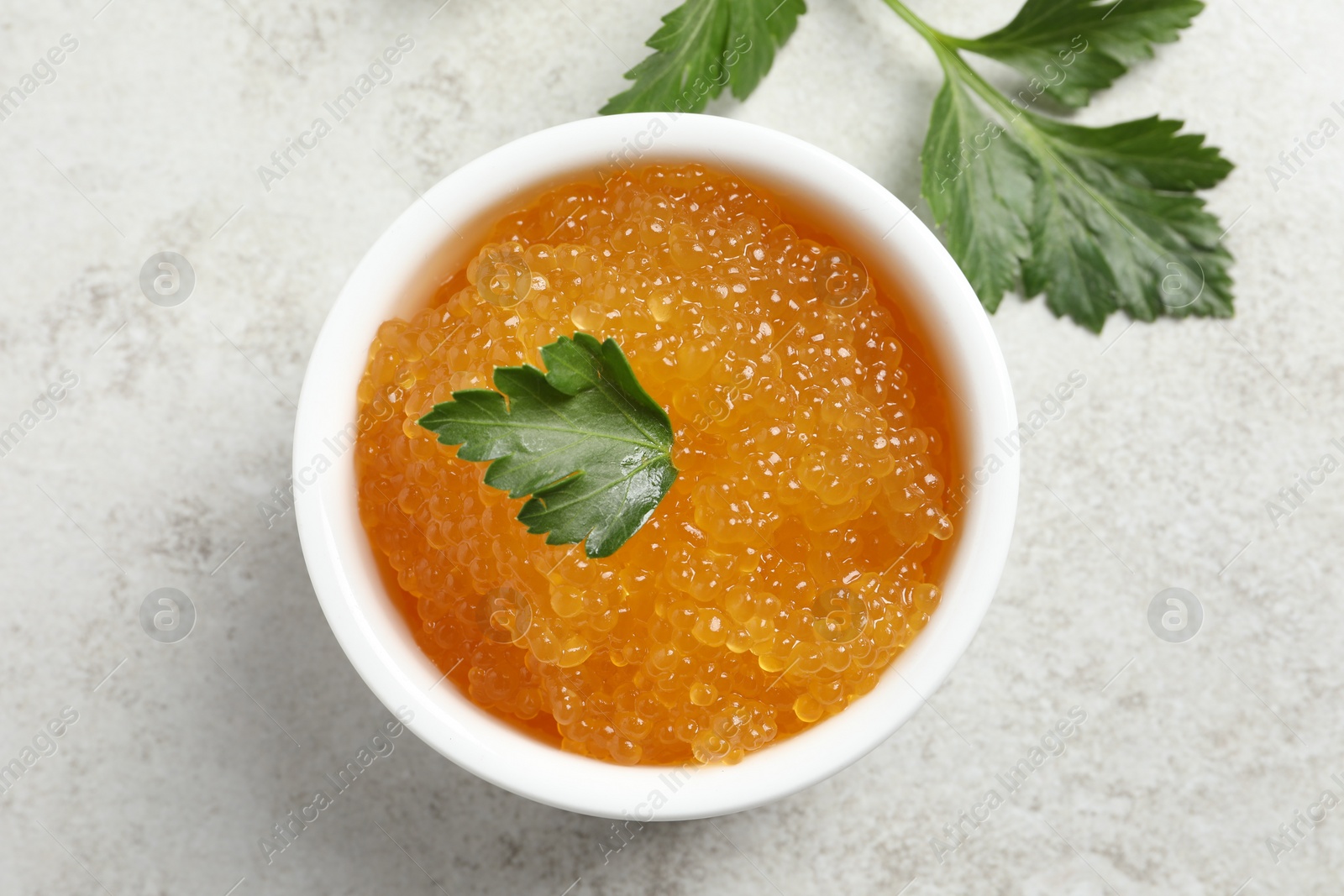 Photo of Fresh pike caviar in bowl and parsley on light grey table, top view