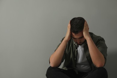 Sad man sitting near light grey wall. Space for text