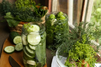 Glass jars, fresh cucumbers and herbs on wooden table indoors. Pickling recipe