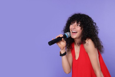 Photo of Beautiful young woman with microphone singing on purple background. Space for text