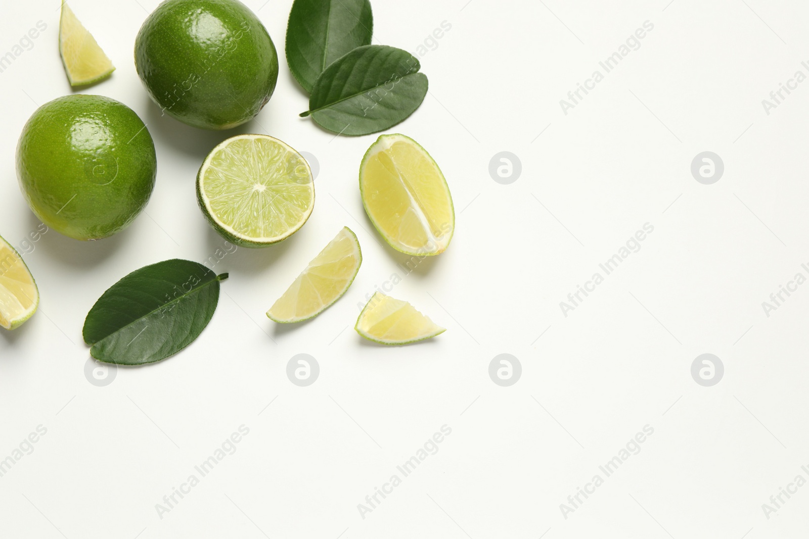 Photo of Whole and cut fresh ripe limes with green leaves on white background, flat lay