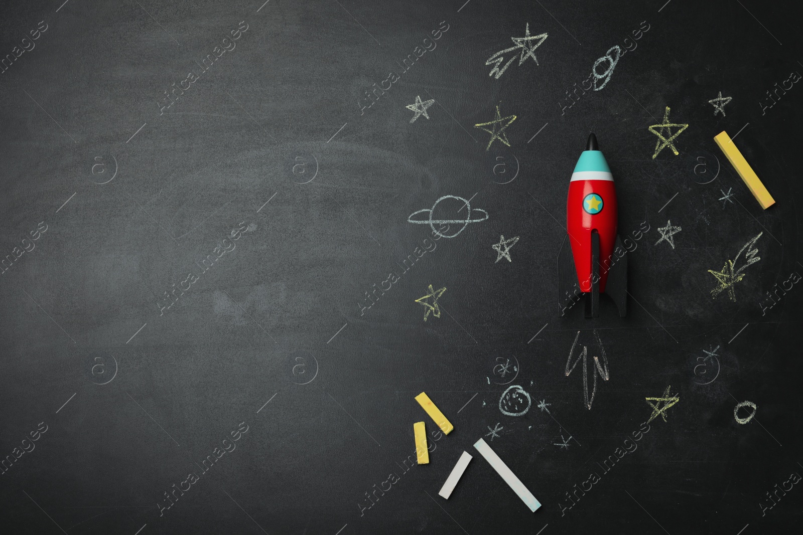 Photo of Bright toy rocket, school supplies and drawings on chalkboard, flat lay. Space for text