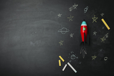 Bright toy rocket, school supplies and drawings on chalkboard, flat lay. Space for text