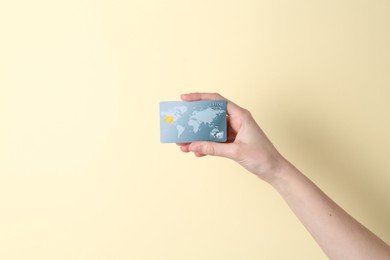 Woman holding credit card on pale yellow background, closeup