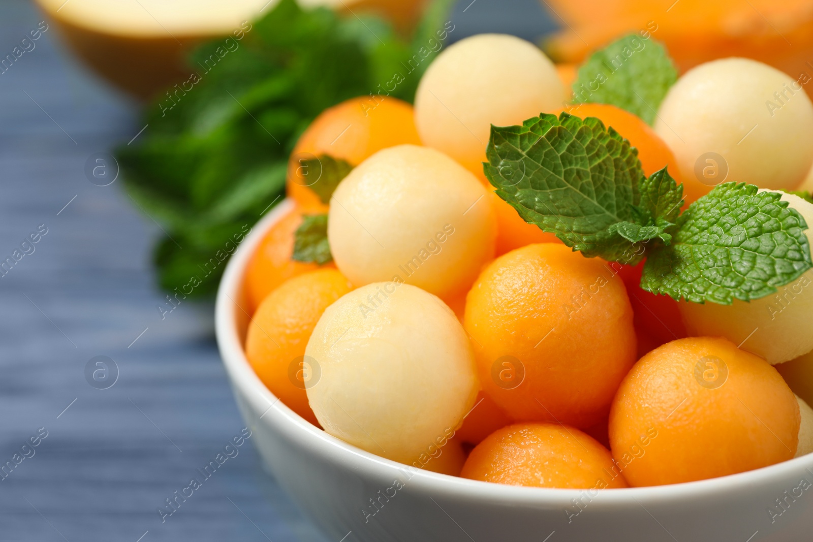 Photo of Melon balls and mint in bowl on blue wooden table, closeup