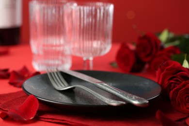 Place setting with roses on red table, closeup. Romantic dinner