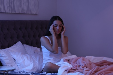 Photo of Young woman suffering from headache while sitting on bed at night. Sleeping problems