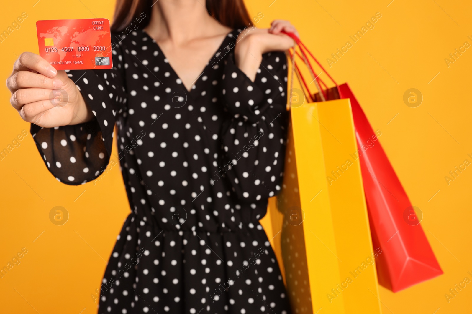 Photo of Woman with shopping bags and credit card on yellow background, closeup