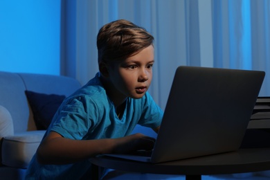 Photo of Shocked little child with laptop in dark room. Danger of internet