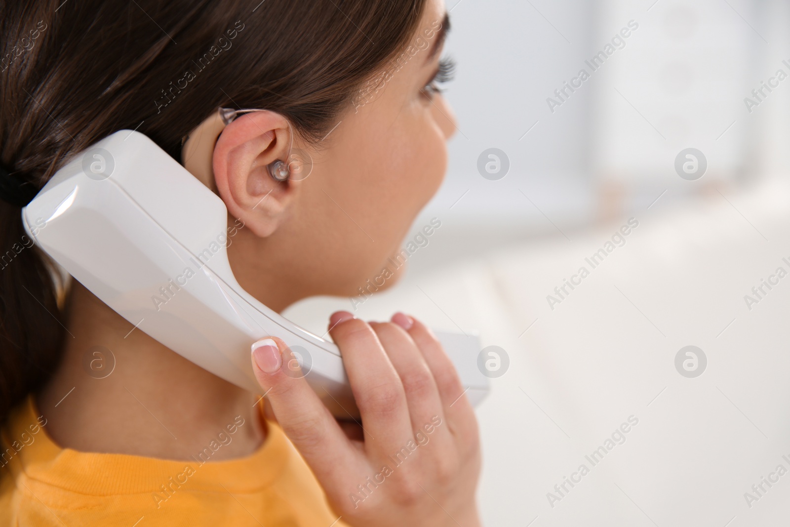Photo of Young woman with hearing aid talking on phone indoors, closeup. Space for text