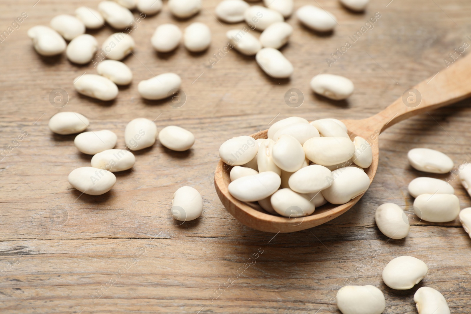 Photo of Raw white beans with spoon on wooden table, closeup