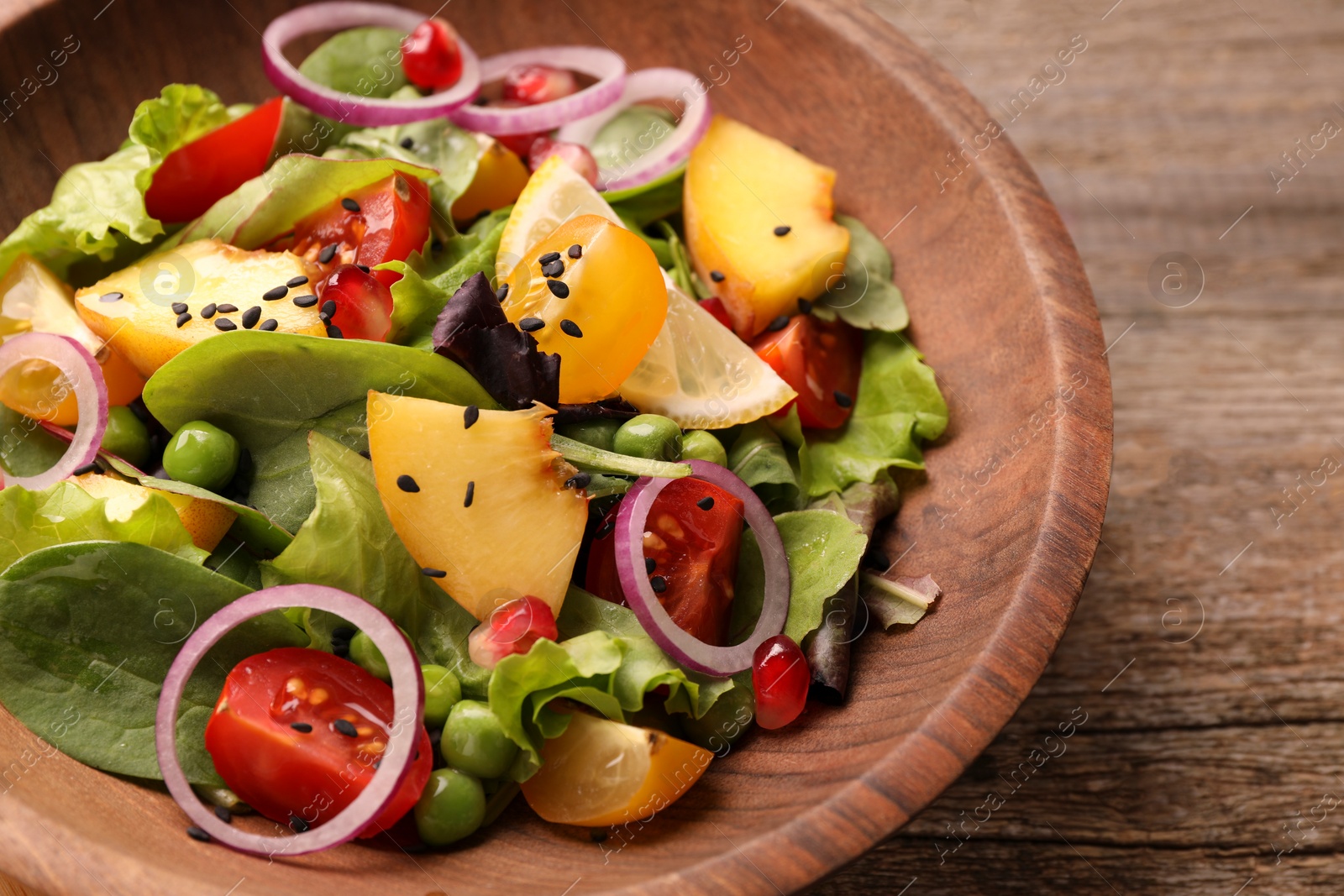 Photo of Delicious salad with peach, green peas and vegetables in bowl on wooden table, closeup