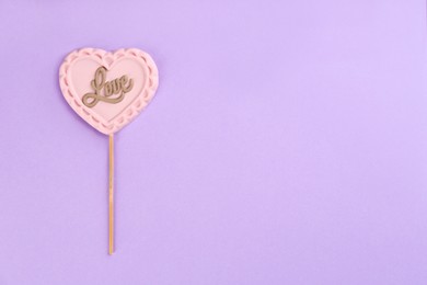 Chocolate heart shaped lollipop with word Love on light lilac background, top view. Space for text