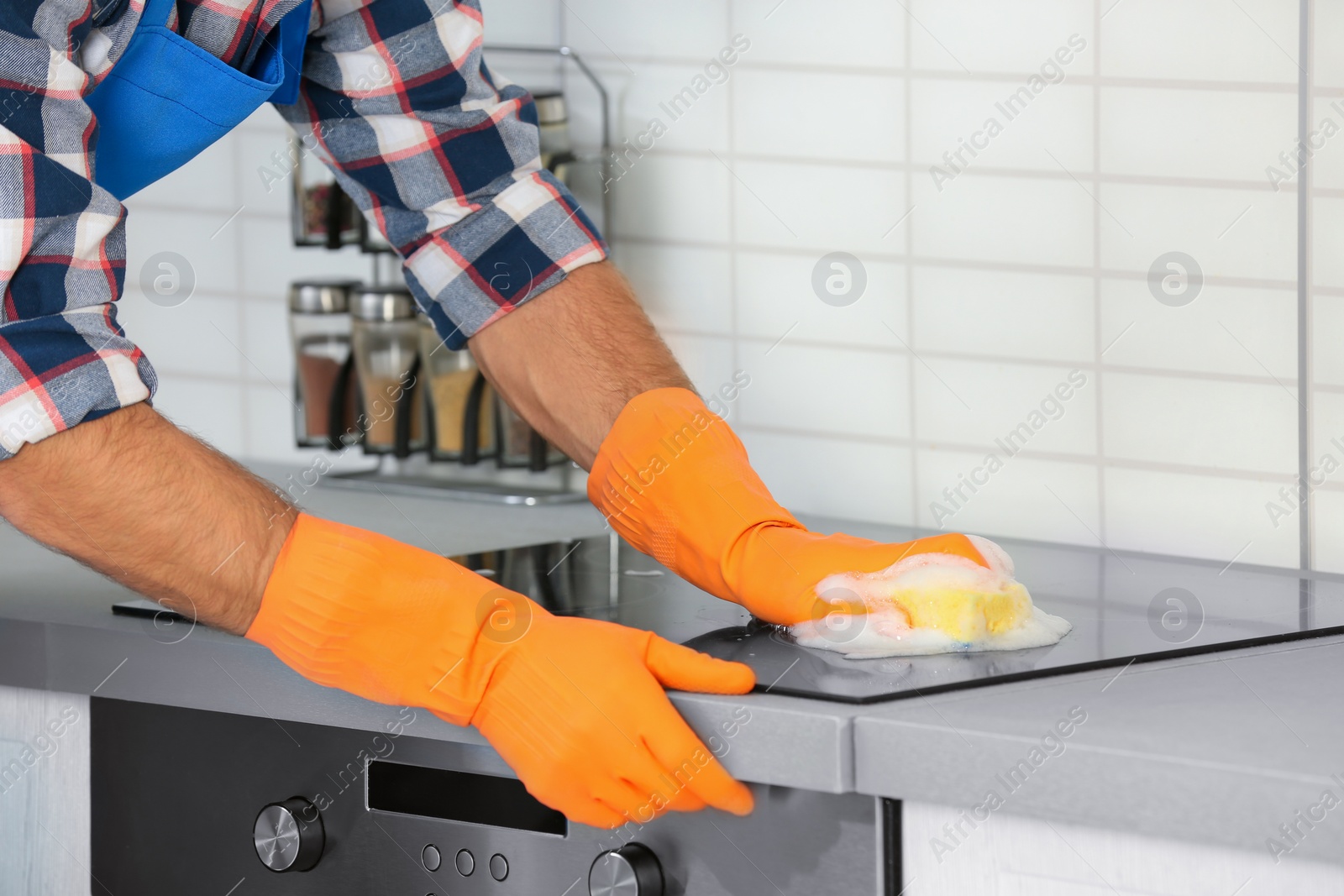 Photo of Man cleaning kitchen stove with sponge, closeup