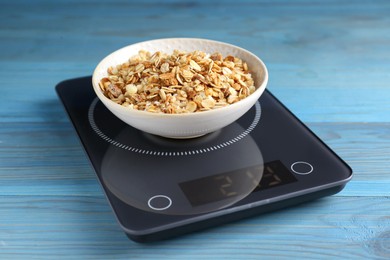 Electronic scales with granola on light blue wooden table, closeup
