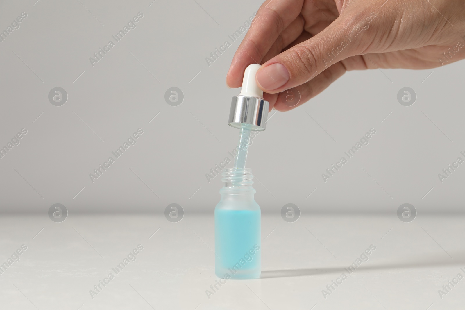 Photo of Woman with cosmetic serum at white table, closeup