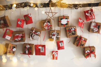 Handmade Advent calendar with gifts hanging on white wall. Christmas season