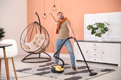 Young man having fun while vacuuming at home