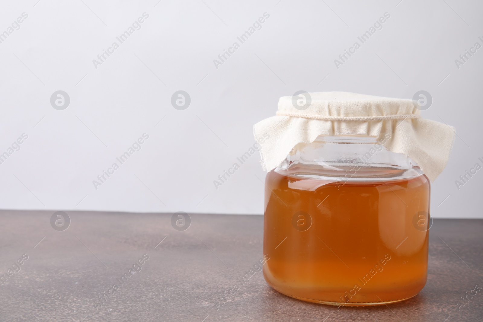 Photo of Homemade fermented kombucha in glass jar on grey table. Space for text