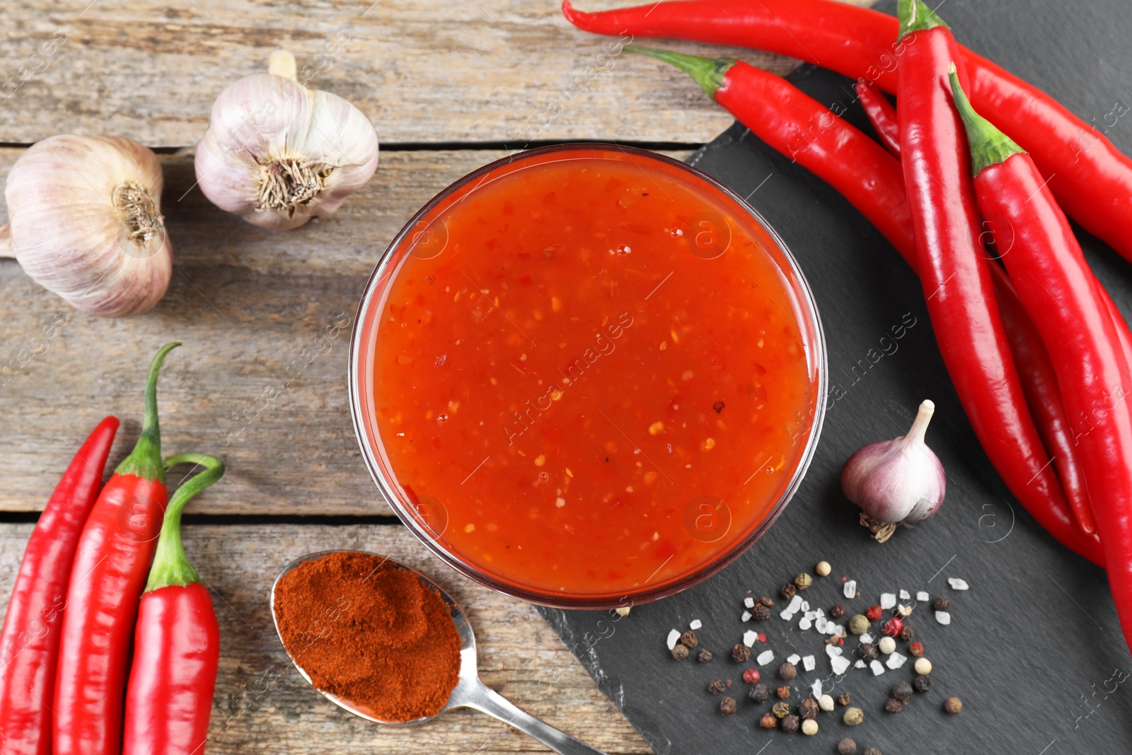 Photo of Spicy chili sauce in bowl and ingredients on wooden table, flat lay