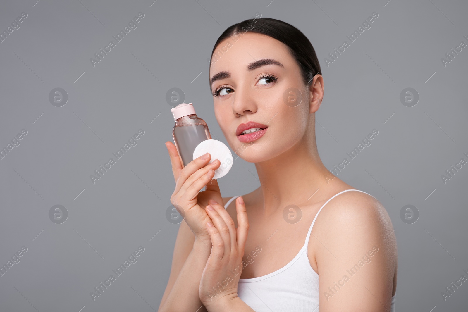 Photo of Beautiful woman with makeup remover and cotton pad on gray background, space for text