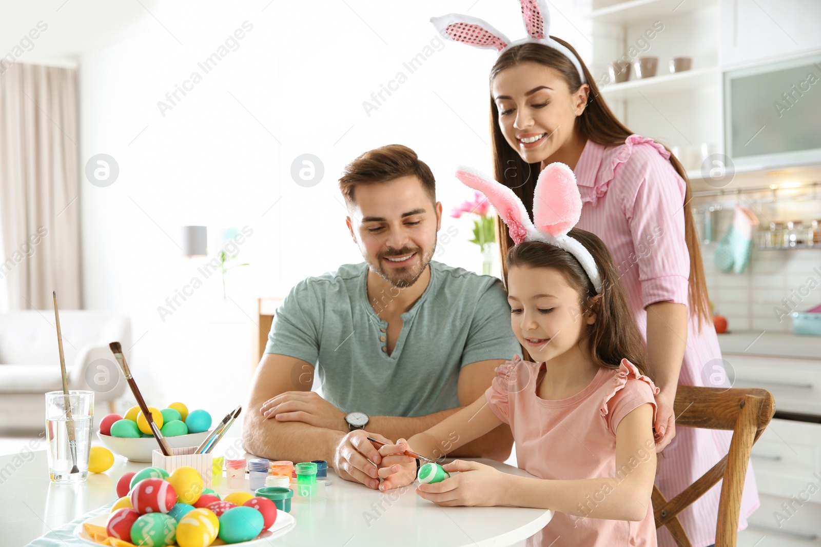 Photo of Father, mother and daughter painting Easter eggs in kitchen, space for text