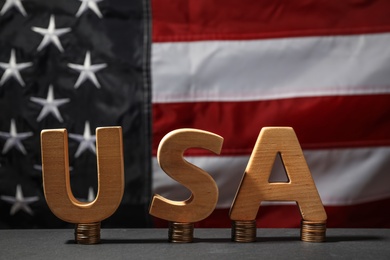Photo of Word USA made with wooden letters and coins on grey table against national flag