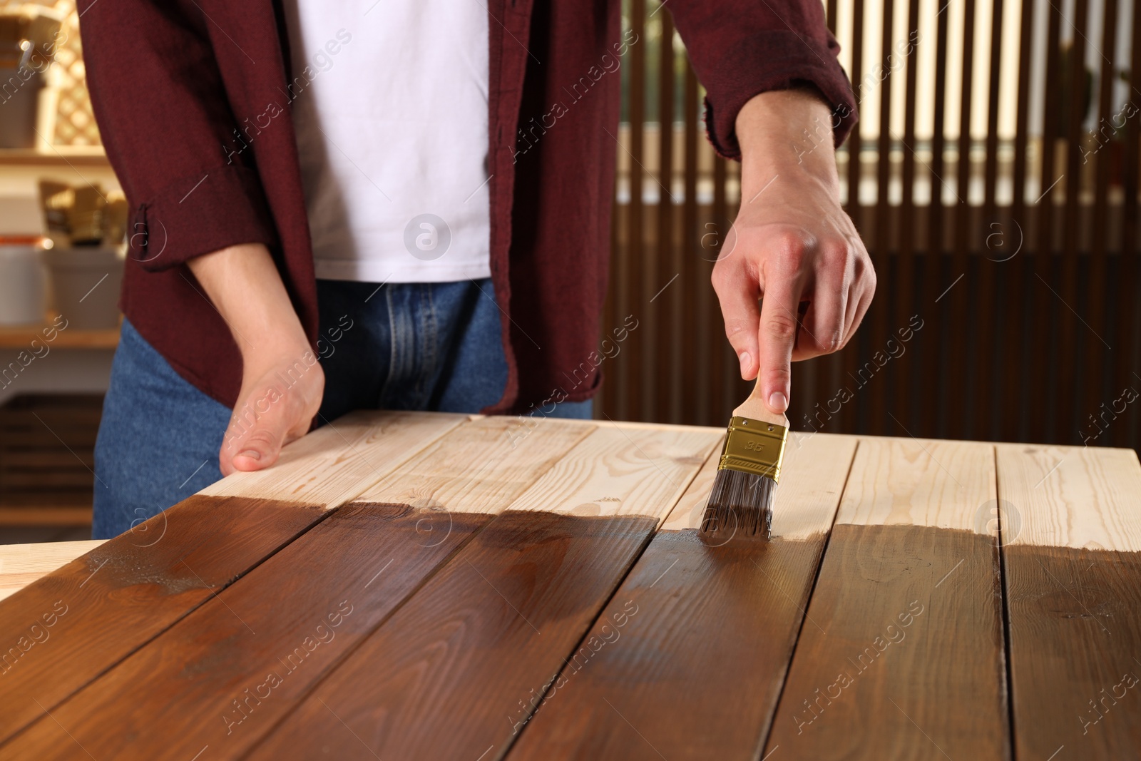 Photo of Man with brush applying wood stain onto wooden surface indoors, closeup