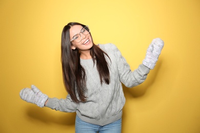 Image of Happy young woman wearing warm sweater and mittens on yellow background