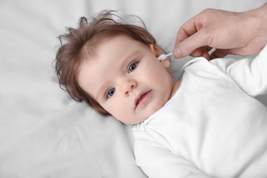 Photo of Father cleaning ear of his baby with cotton bud on bed, closeup