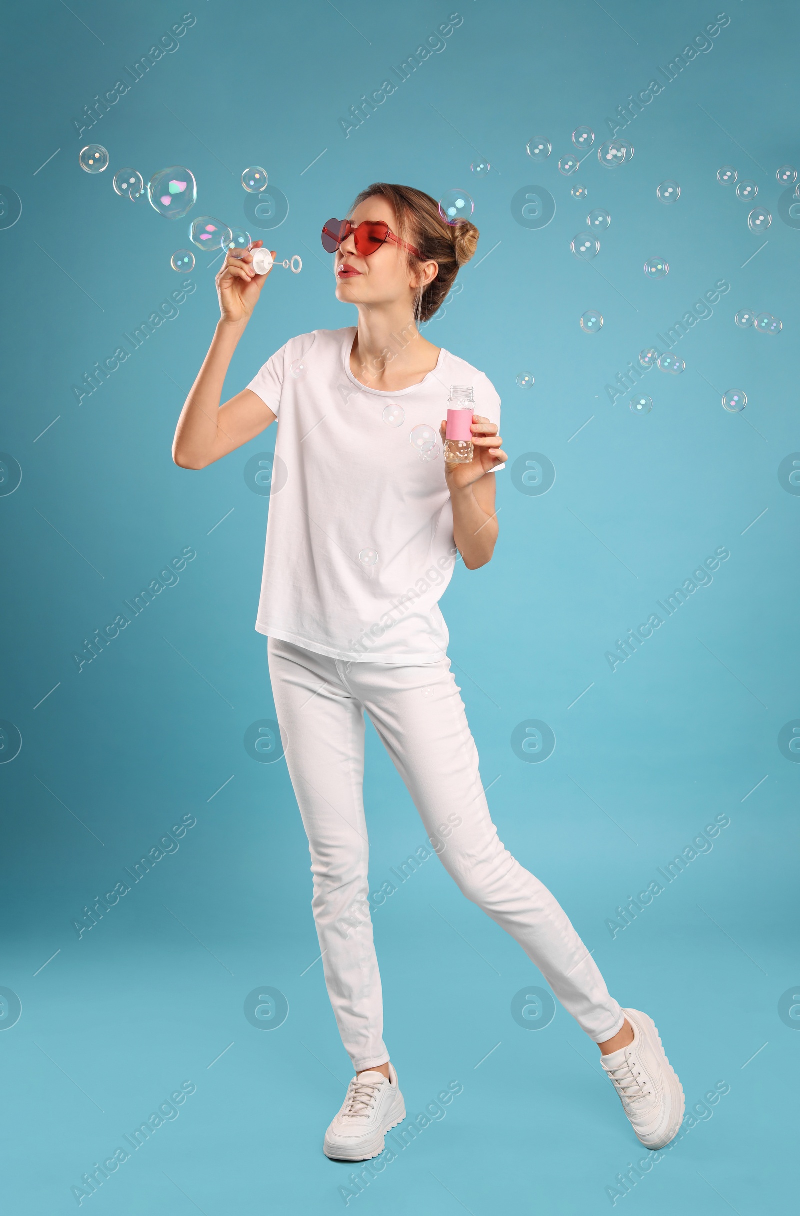 Photo of Young woman blowing soap bubbles on light blue background