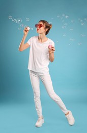 Young woman blowing soap bubbles on light blue background