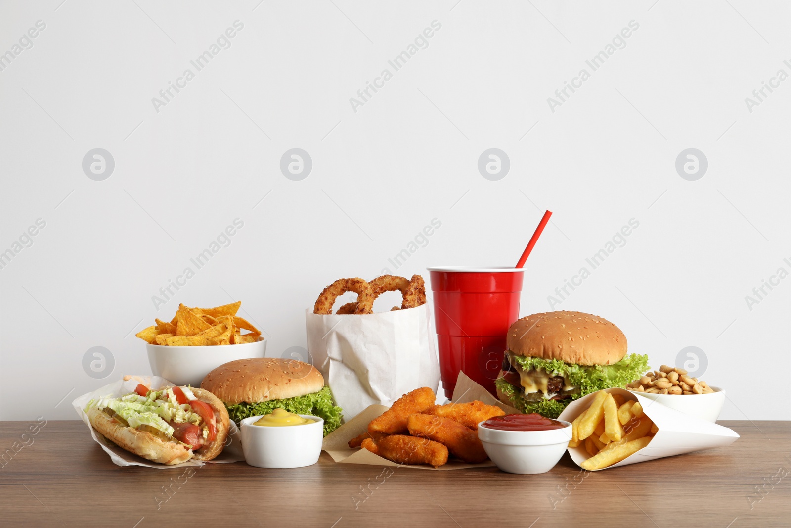 Photo of French fries, burgers and other fast food on wooden table against white background