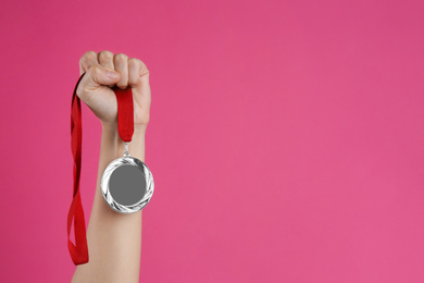 Photo of Woman holding silver medal on pink background, closeup. Space for design