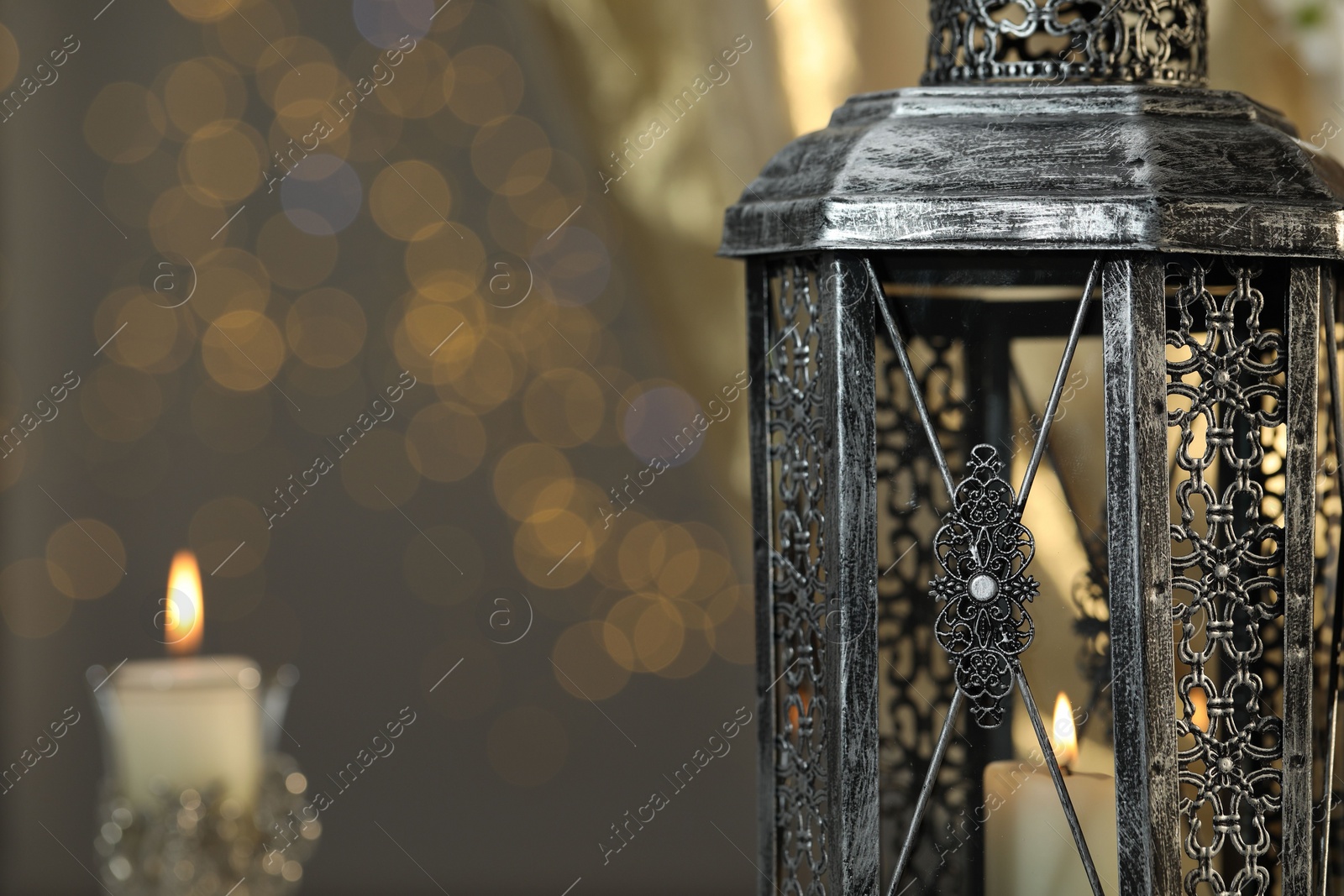 Photo of Arabic lantern and burning candles against blurred lights, space for text