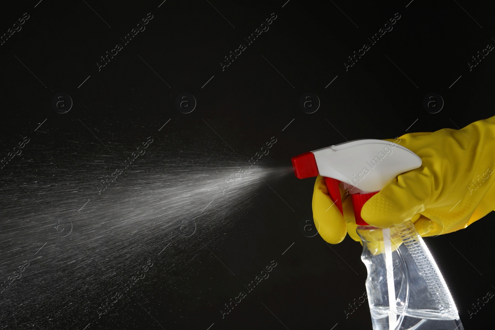 Photo of Woman spraying liquid from bottle on black background, closeup