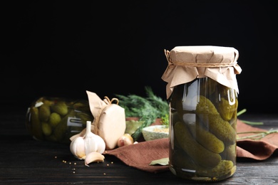 Jars with pickled cucumbers on wooden table against black background, space for text