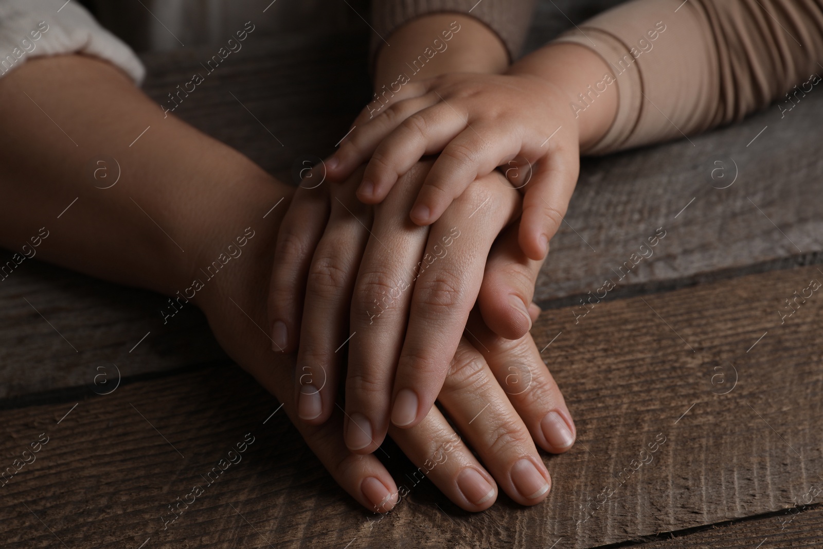 Photo of Family holding hands together at wooden table, closeup