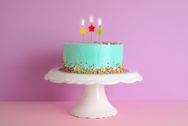 Photo of Fresh delicious birthday cake with candles on stand against color background