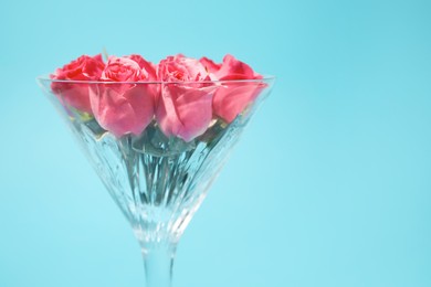 Photo of Beautiful martini glass with pink roses on light blue background, closeup. Space for text