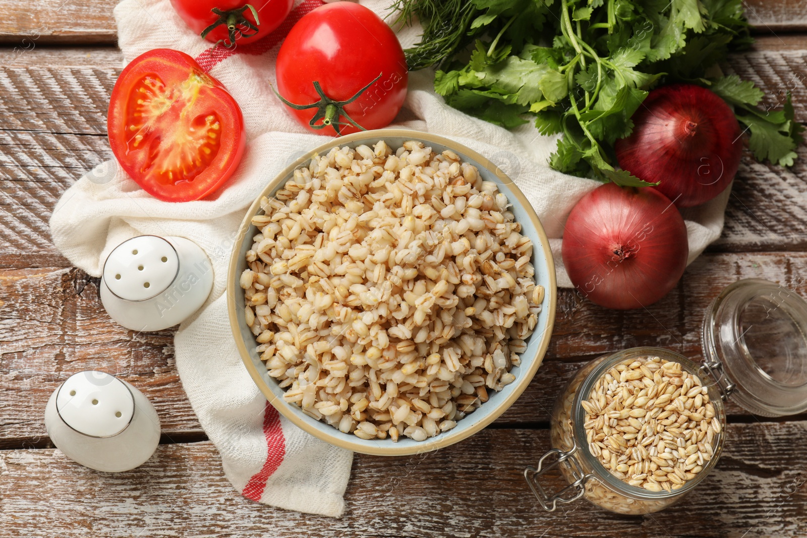 Photo of Delicious pearl barley in bowl served on wooden table, flat lay