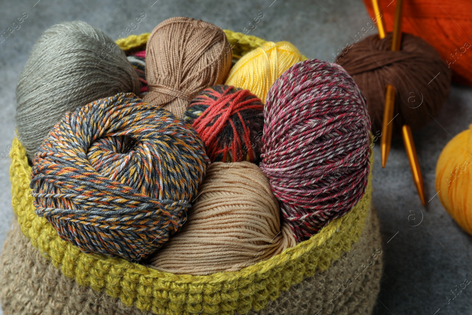 Photo of Soft woolen yarns and knitting needles on grey table, closeup